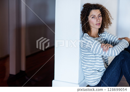 Sitting woman hugging knees on hardwood floor in hallway, with square column, copy space Sitting woman hugging knees on hardwood floor in hallway, with square column, copy space 128699054