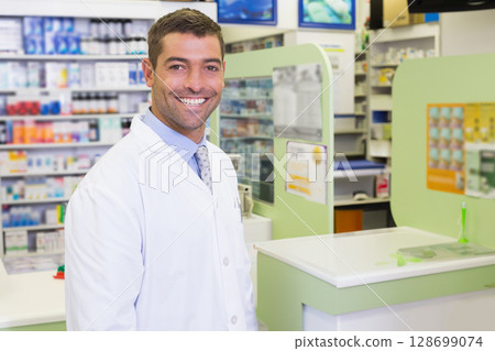 Smiling male pharmacist standing at counter in pharmacy, with medications and posters, copy space Smiling male pharmacist standing at counter in pharmacy, with medications and posters, copy space 128699074