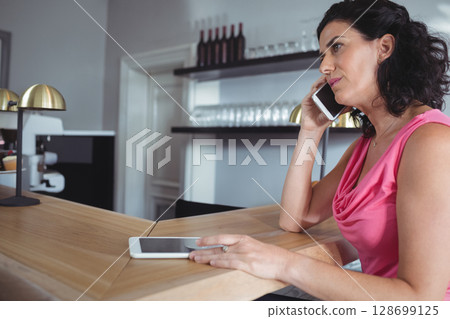 Talking woman on smartphone at cafe counter, with tablet, espresso machine, copy space Talking woman on smartphone at cafe counter, with tablet, espresso machine, copy space 128699125
