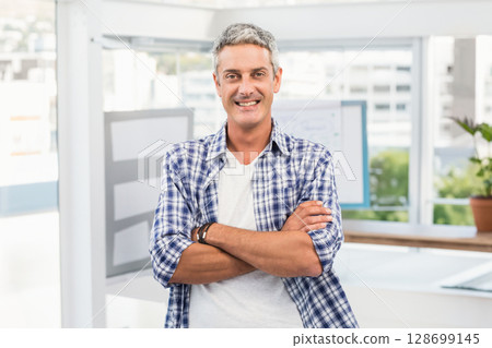 Standing man crossing arms and smiling in bright office, with whiteboard, plant and large windows Standing man crossing arms and smiling in bright office, with whiteboard, plant and large windows 128699145
