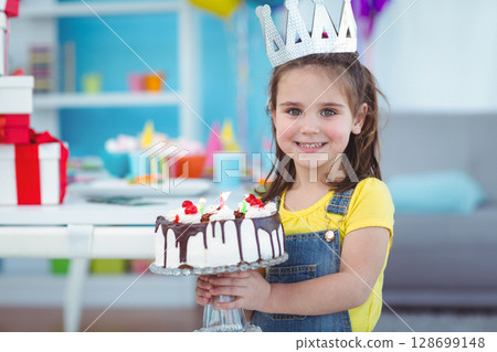 Smiling child wearing paper crown holding frosted cake and gift boxes at birthday party, copy space 128699148