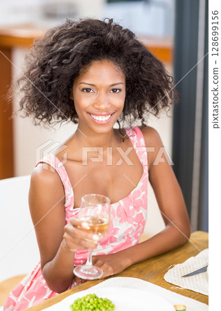 Smiling mid-adult African American woman holding wine glass at wooden dining table, with green peas 128699156