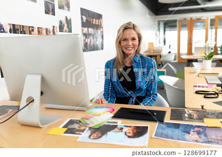 Working woman arranging photos and color swatches on desk in studio, with graphics tablet 128699177