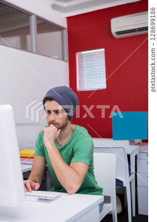 Thinking man in his 20s resting chin at open-plan desk, with computer and folders, copy space 128699186