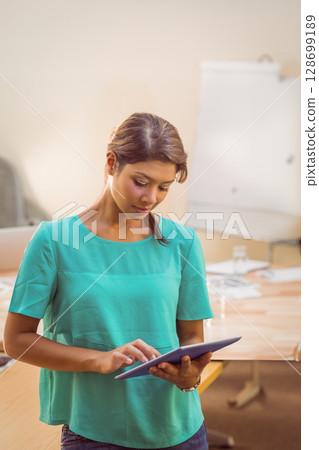 Standing Indian woman holding tablet in modern conference room, showing flip chart and papers 128699189