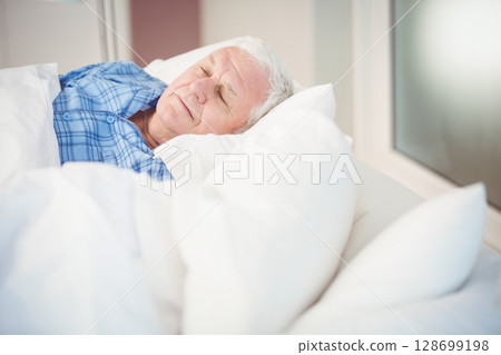 Resting senior man lying on side in bedroom, with white duvet and blue pajamas, copy space Resting senior man lying on side in bedroom, with white duvet and blue pajamas, copy space 128699198