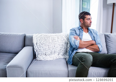 Sitting man looking outside on grey sofa in living room, with knitted blanket, copy space 128699201