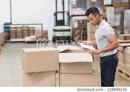 Inspecting man holding clipboard and pen in warehouse, with forklift and boxes, copy space Inspecting man holding clipboard and pen in warehouse, with forklift and boxes, copy space 128699230