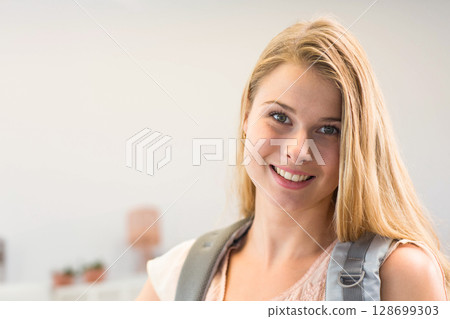Smiling teenage girl wearing gray backpack standing indoors, with tiny plants and lamp, copy space 128699303