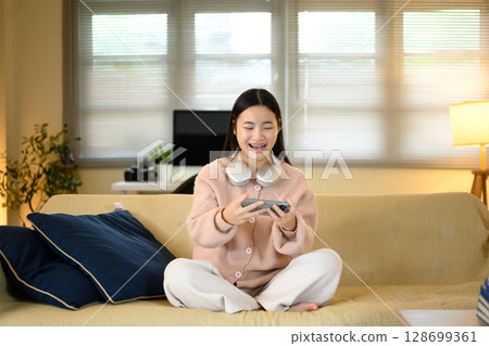 Cheerful teenage girl playing games on her smartphone while relaxing on a sofa at home 128699361