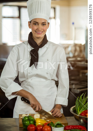Slicing mushrooms female chef using knife on cutting board in commercial kitchen, with vegetables Slicing mushrooms female chef using knife on cutting board in commercial kitchen, with vegetables 128699376