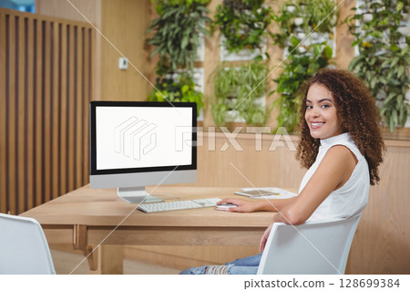 Smiling woman working at desk in modern coworking space, with computer and notebook, copy space Smiling woman working at desk in modern coworking space, with computer and notebook, copy space 128699384