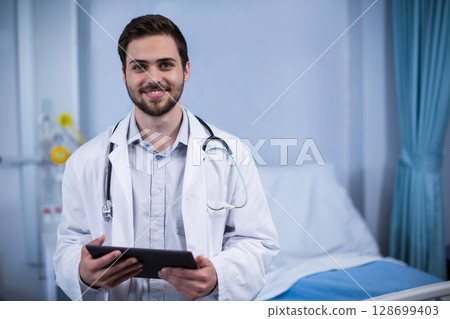 Male doctor wearing lab coat and stethoscope, holding digital tablet in hospital room Male doctor wearing lab coat and stethoscope, holding digital tablet in hospital room 128699403