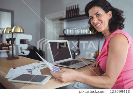 Smiling businesswoman reviewing charts at modern cafe with laptop tablet and coffee, copy space 128699418