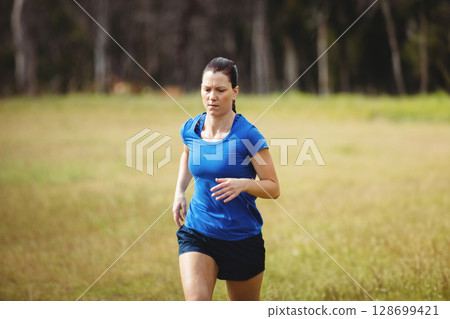 Running athletic woman crossing open grassy field at forest edge, with running shoes Running athletic woman crossing open grassy field at forest edge, with running shoes 128699421