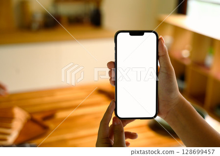 Close up of hands holding smartphone with a blank screen in a modern kitchen 128699457