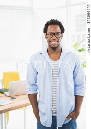 Leaning man placing hands in pockets at wooden desk in office, with laptop phone scattered papers Leaning man placing hands in pockets at wooden desk in office, with laptop phone scattered papers 128699493