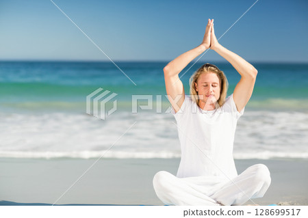 Meditating man raising hands above head on sandy beach shore with turquoise ocean, copy space Meditating man raising hands above head on sandy beach shore with turquoise ocean, copy space 128699517