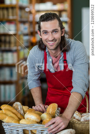 Smiling man leaning on counter in small bakery, with wicker baskets of fresh bread 128699522