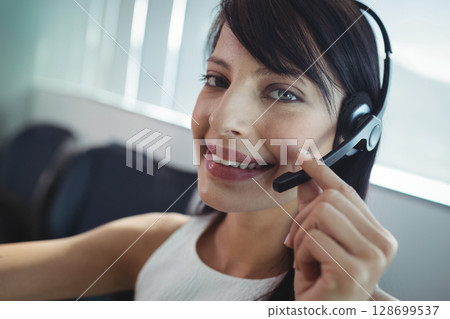 Smiling woman adjusting black boom headset at call center, featuring office chairs, copy space Smiling woman adjusting black boom headset at call center, featuring office chairs, copy space 128699537