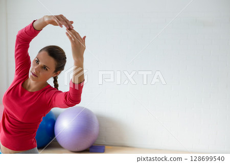 Stretching woman leaning sideways in yoga studio, with purple and blue exercise balls, copy space 128699540