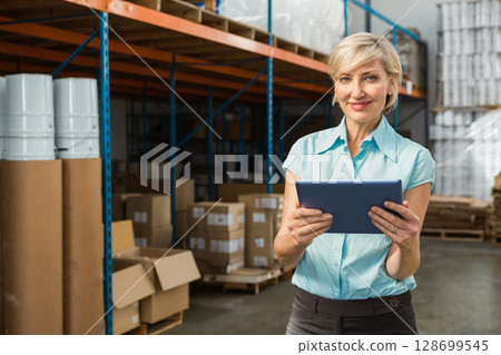 Senior woman holding tablet checking inventory in warehouse with boxes and pallets, copy space Senior woman holding tablet checking inventory in warehouse with boxes and pallets, copy space 128699545