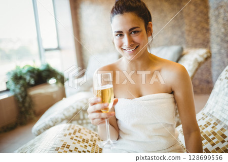 Relaxing woman holding champagne flute on mosaic chaise lounge in spa, with potted plant 128699556