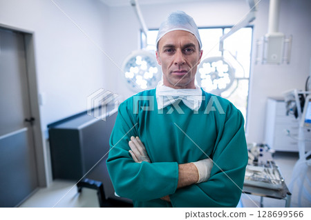 Standing male surgeon wearing bouffant cap in operating room, with surgical light and instruments 128699566