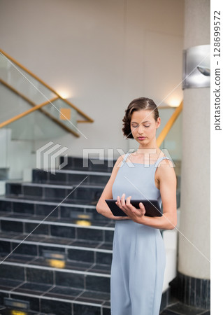 Businesswoman studying financial report on black tablet in corporate lobby, copy space 128699572