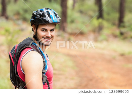 Smiling male cyclist turning head on pine forest trail, with helmet and backpack, copy space Smiling male cyclist turning head on pine forest trail, with helmet and backpack, copy space 128699605