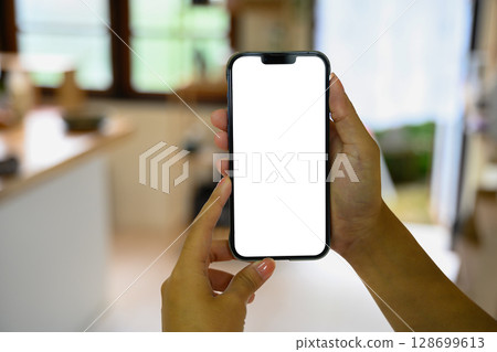 Hands holding smartphone with a blank screen in a modern kitchen 128699613