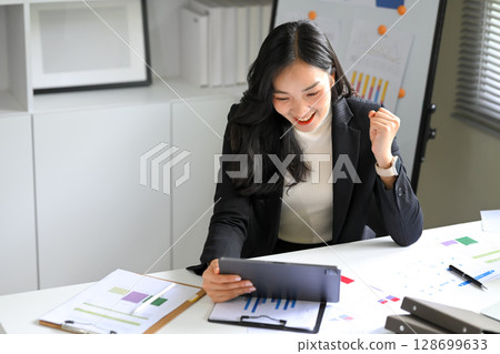 Happy female executive celebrating sales results while viewing analytics on tablet 128699633