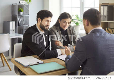 Couple sitting at the desk discussing contract and having consultation with man realtor in office. 128700303