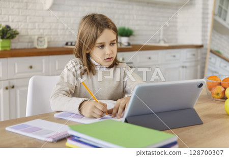 Child using tablet for homework, diligent school student sitting alone at kitchen table at home Child using tablet for homework, diligent school student sitting alone at kitchen table at home 128700307