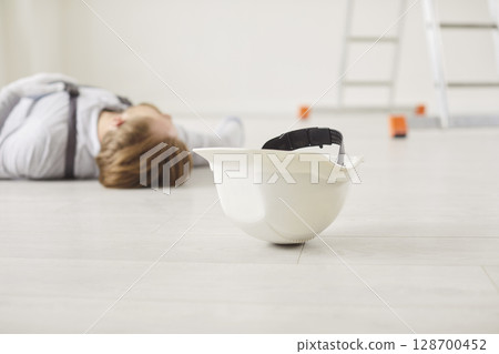 Unconscious construction worker lying on floor in overall after job accident on workplace. Unconscious construction worker lying on floor in overall after job accident on workplace. 128700452