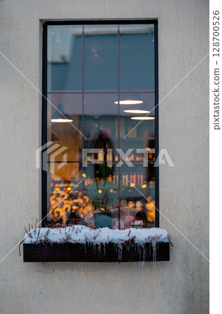 a lighted window with a snow-covered flower box in the wall of a masonry building 128700526