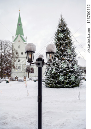Snowy lantern with decorated Christmas tree and church in blurred background, shallow DOF 128700532