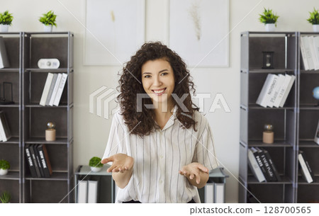 Curly haired female office worker shrugging shoulders having indecisive expression posing in cabinet Curly haired female office worker shrugging shoulders having indecisive expression posing in cabinet 128700565