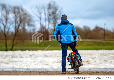 A man on an electric unicycle stands by the river and watches the ice break in the spring 128700635