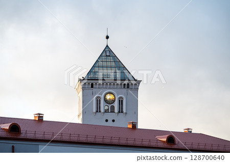 A tower with a clock and a fragment of a modern building on the background of the sunset sky. 128700640