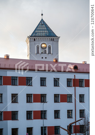 A tower with a clock and a fragment of a modern building on the background of the sunset sky. 128700641
