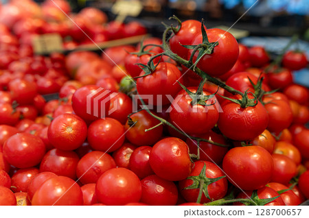 Bright red tomatoes piled high in a bustling market filled with fresh produce. 128700657