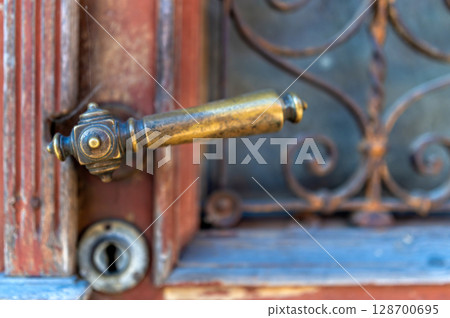 Close-up of a brass door handle and lock on a vintage wooden door with ironwork details. 128700695