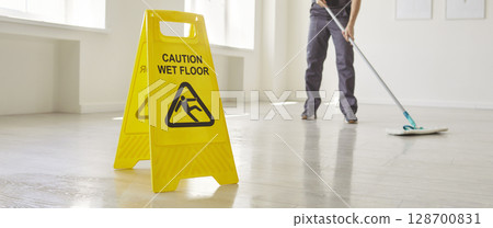 Yellow Caution Wet Floor sign warning of hazardous surface, person mopping floor indoor Yellow Caution Wet Floor sign warning of hazardous surface, person mopping floor indoor 128700831