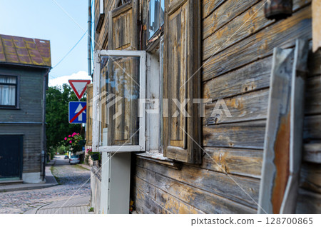 A weathered wooden building with an open window and nearby street signs in a quaint neighborhood 128700865