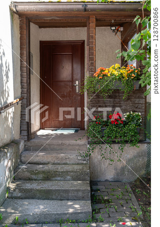 A cozy entrance features colorful flowers in pots alongside a rustic wooden door. 128700866