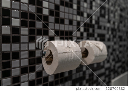 Two rolls of toilet paper displayed on a chrome holder in a modern bathroom setting. Two rolls of toilet paper displayed on a chrome holder in a modern bathroom setting. 128700882