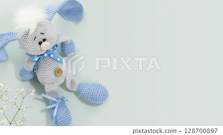 Handmade crochet rabbit toy on blue background with white flowers and copy space. Handmade Easter Bunny Soft Toys Handmade crochet rabbit toy on blue background with white flowers and copy space. Handmade Easter Bunny Soft Toys 128700897