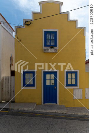 Bright yellow house with blue accents and a balcony in a quaint neighborhood on a sunny day 128700910