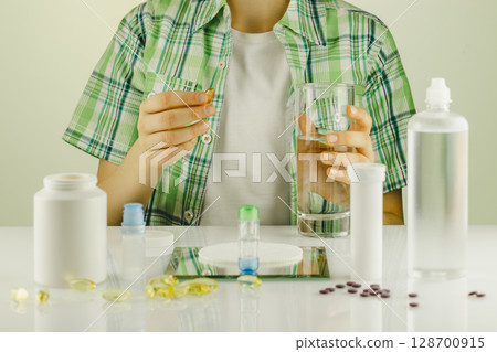 Ophthalmology concept with boy siting at the table with containers with contact lenses, eye drops, clean solutions, supplements and vitamins for good vision. Eye care and eye treatment 128700915